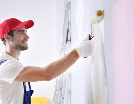 Young worker painting wall in room